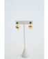 Gold heart-shaped earrings with an emerald green stone stud on a white stand against a light gray background