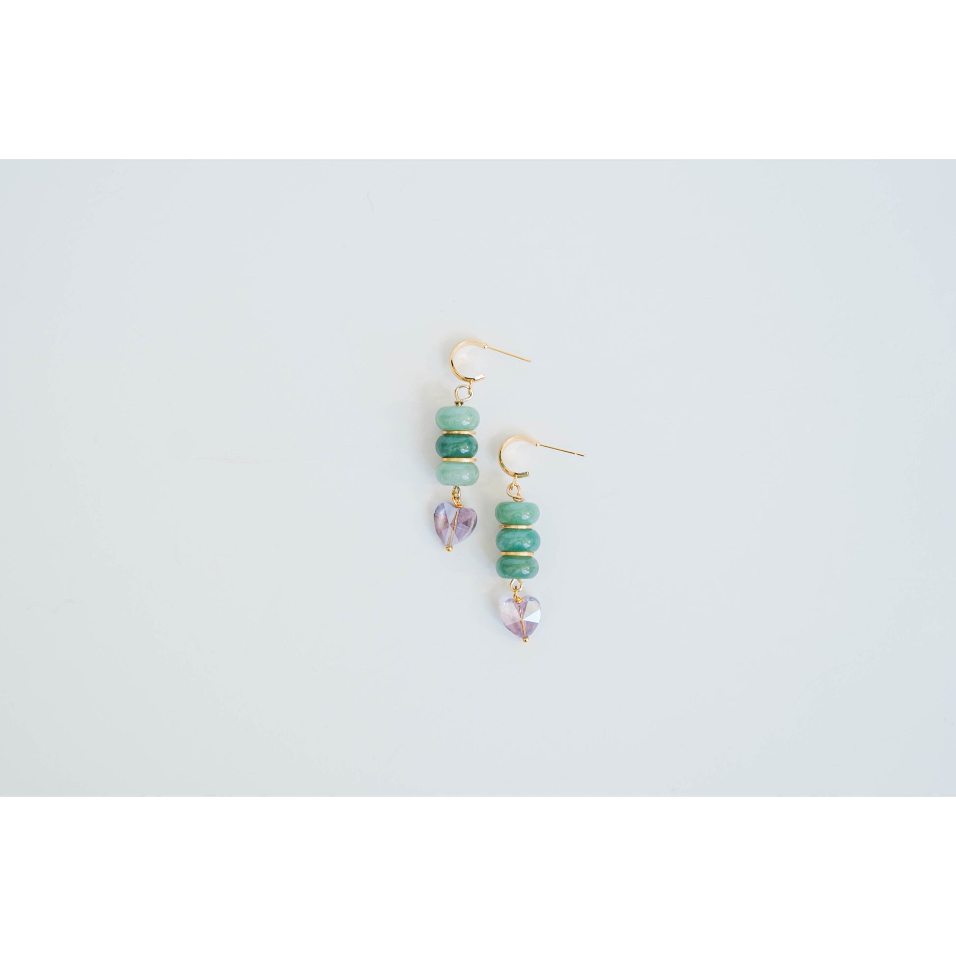 Pair of gold dangle earrings with green jade beads and gold spacers and purple crystal heart accents on a light gray background