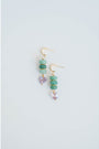 Pair of gold dangle earrings with green jade beads and gold spacers and purple crystal heart accents on a light gray background