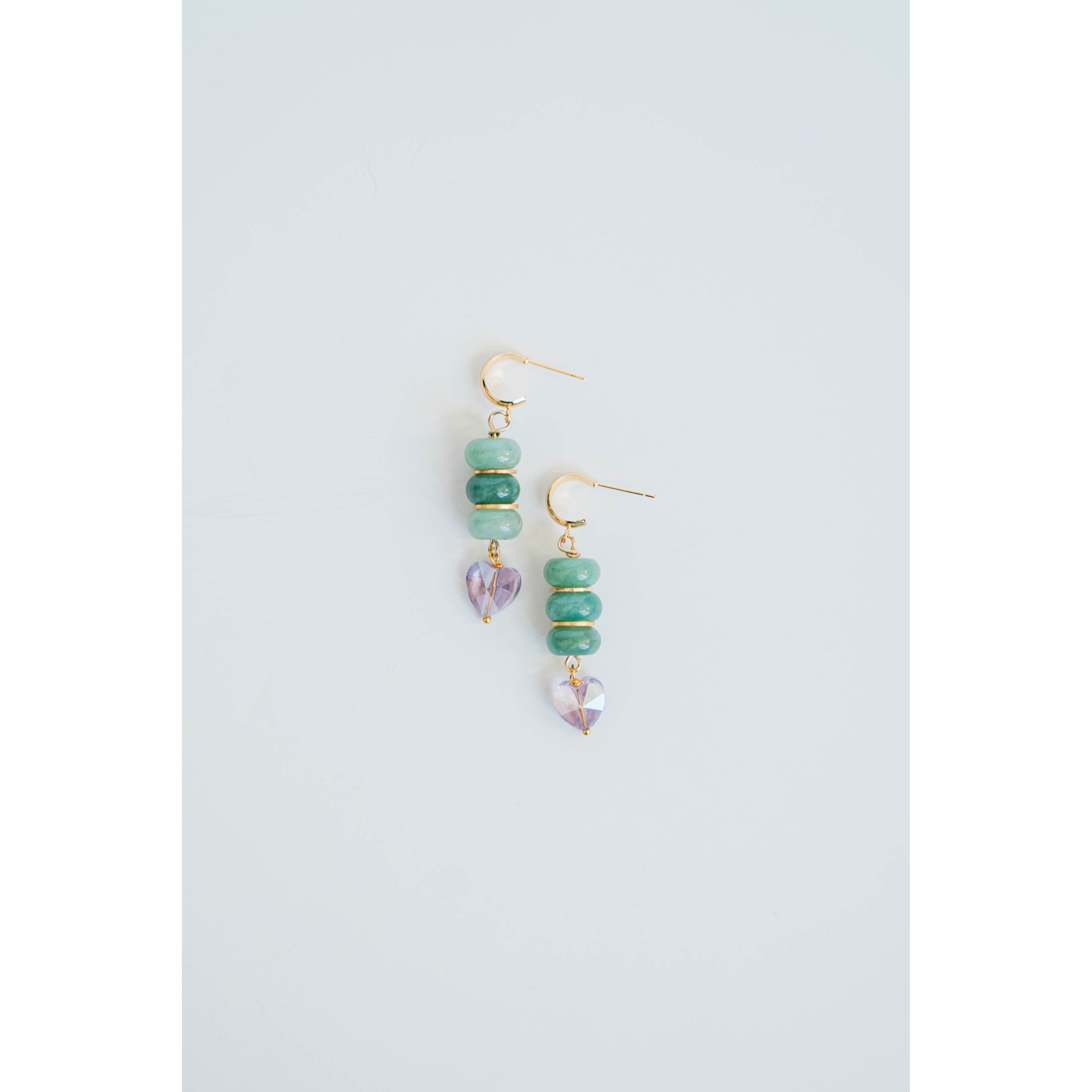 Pair of gold dangle earrings with green jade beads and gold spacers and purple crystal heart accents on a light gray background