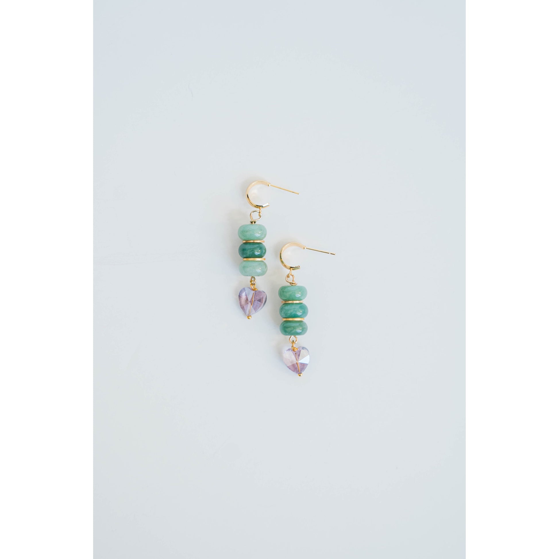 Pair of gold dangle earrings with green jade beads and gold spacers and purple crystal heart accents on a light gray background