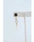 Gold chain earring with black gemstone and white heart pendant on a light gray background