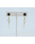 Pair of gold dangle earrings with black gemstones and white heart pendants on a light grey background
