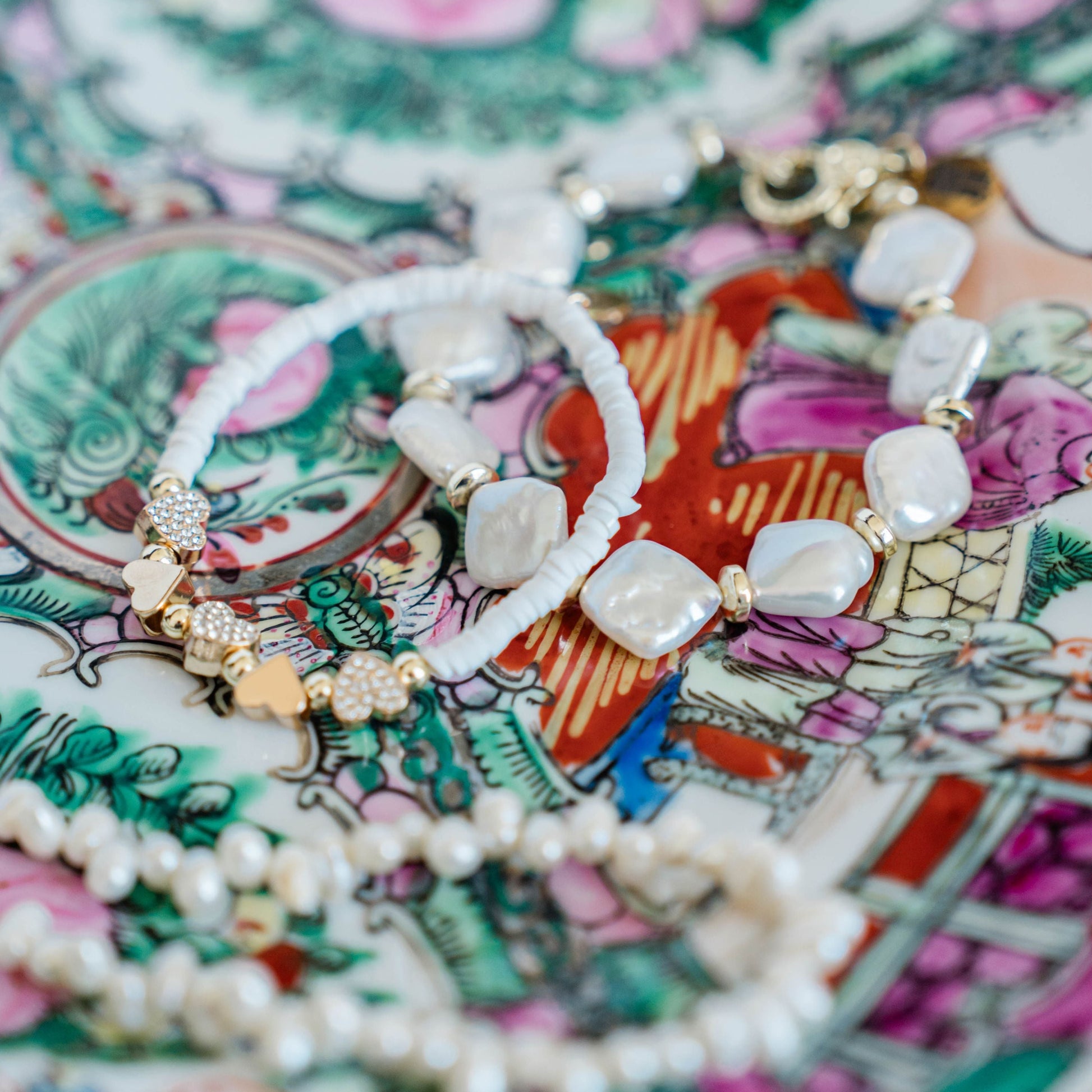 two bracelets with white beads and pearls and gold accents on a multicolor vintage plate