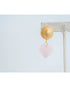 earring with large gold textured circular posts and  a light pink quartz heart dangle accent on an earring stand on a light background
