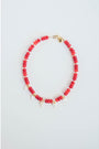 Necklace with red beads, gold spacers, white pearl heart charms and a gold pave clasp on a light gray background