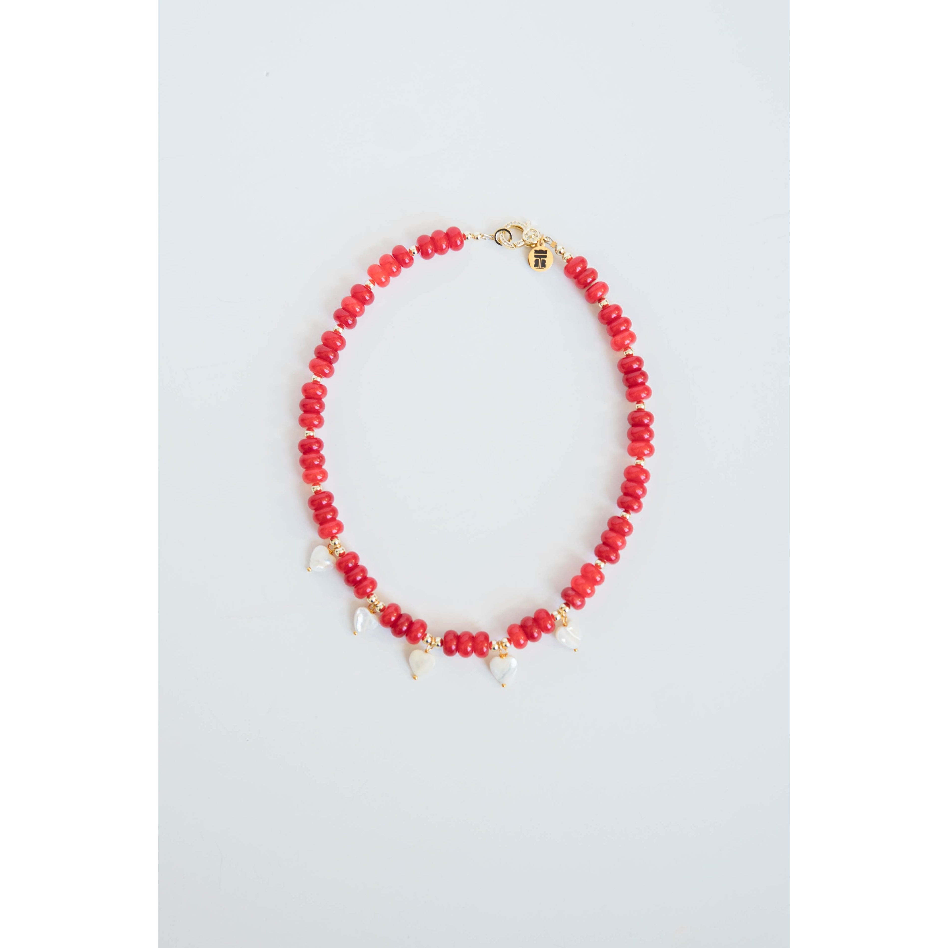 Necklace with red beads, gold spacers, white pearl heart charms and a gold pave clasp on a light gray background