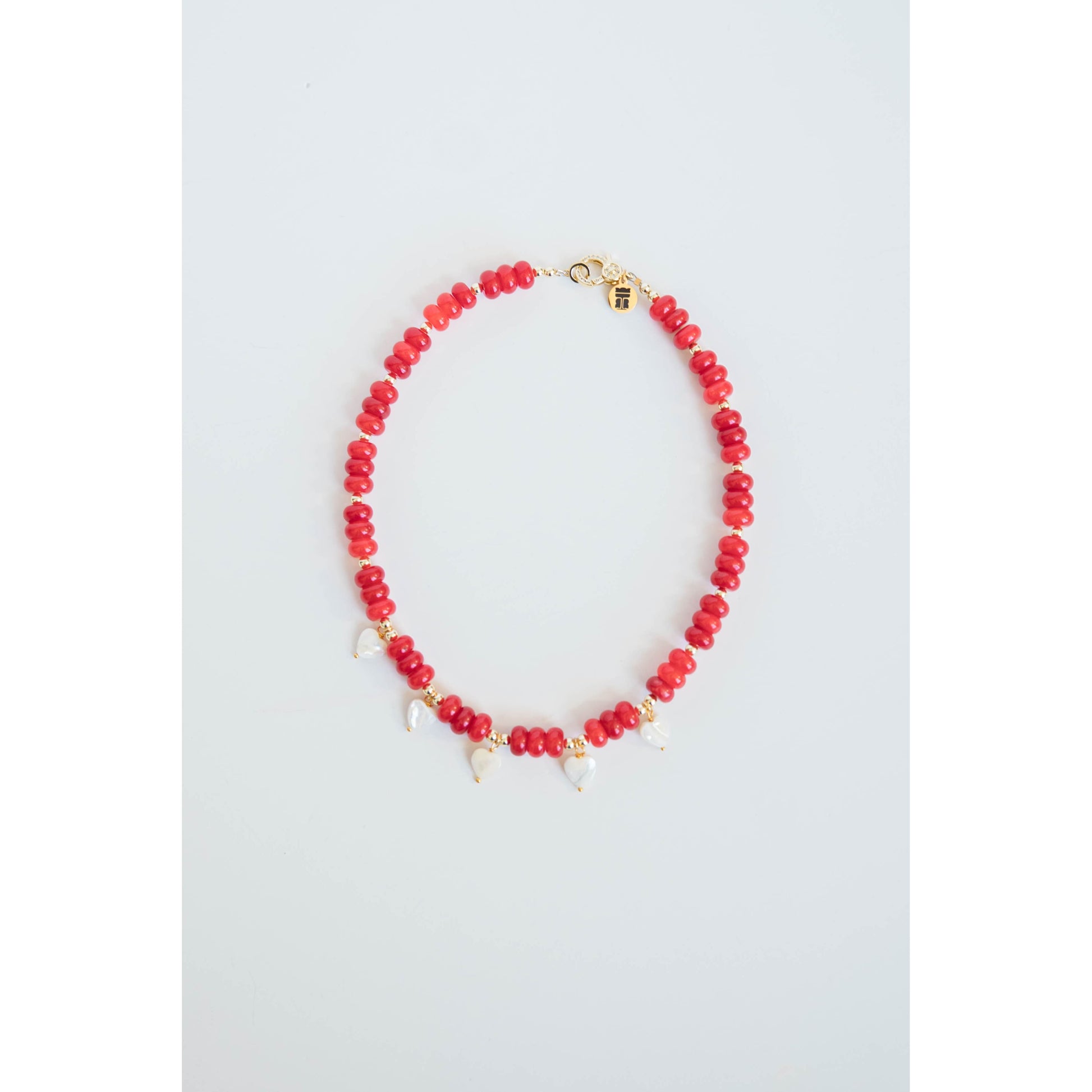 Necklace with red beads, gold spacers, white pearl heart charms and a gold pave clasp on a light gray background