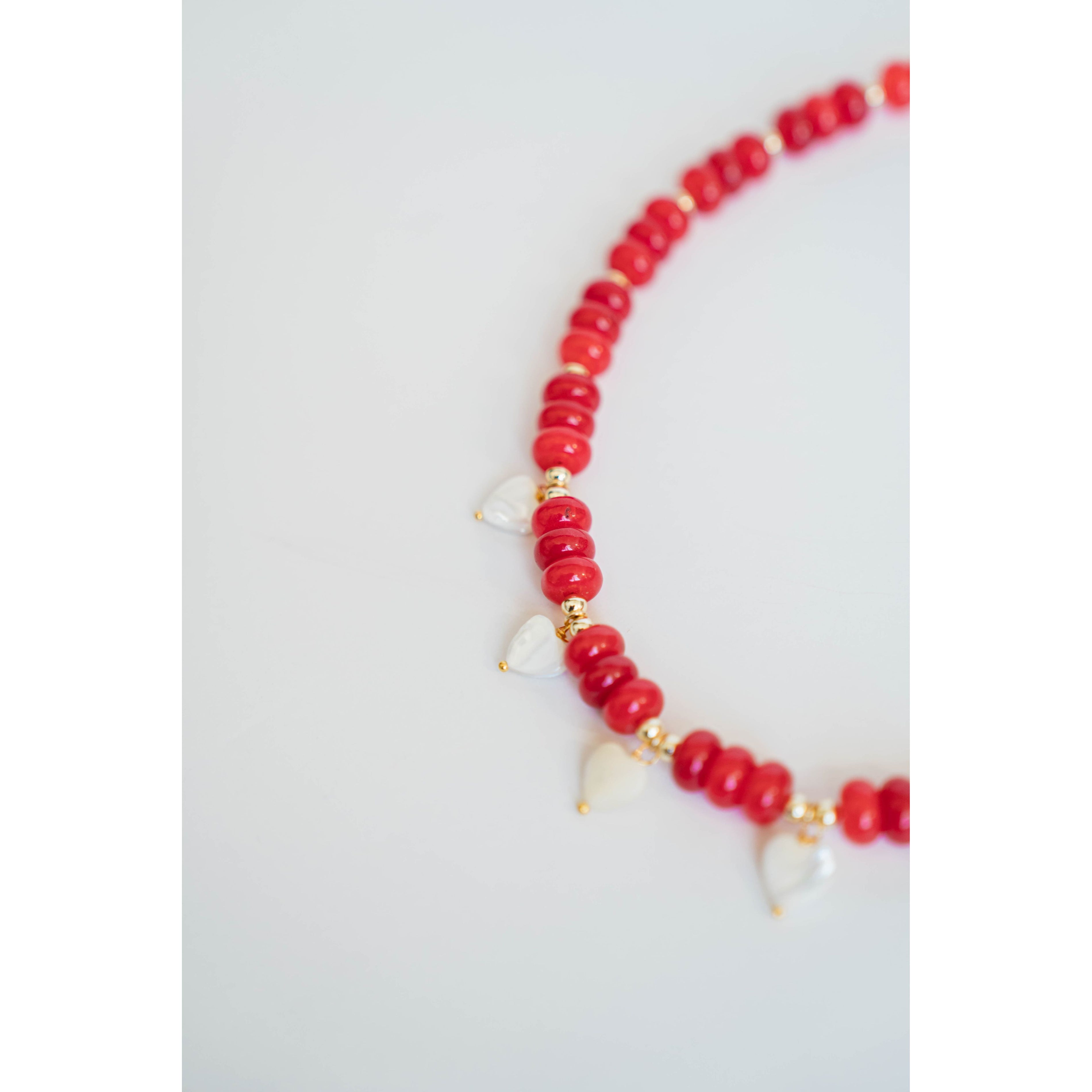 necklace with red beads, gold spacers, and white pearl heart charms on a light background