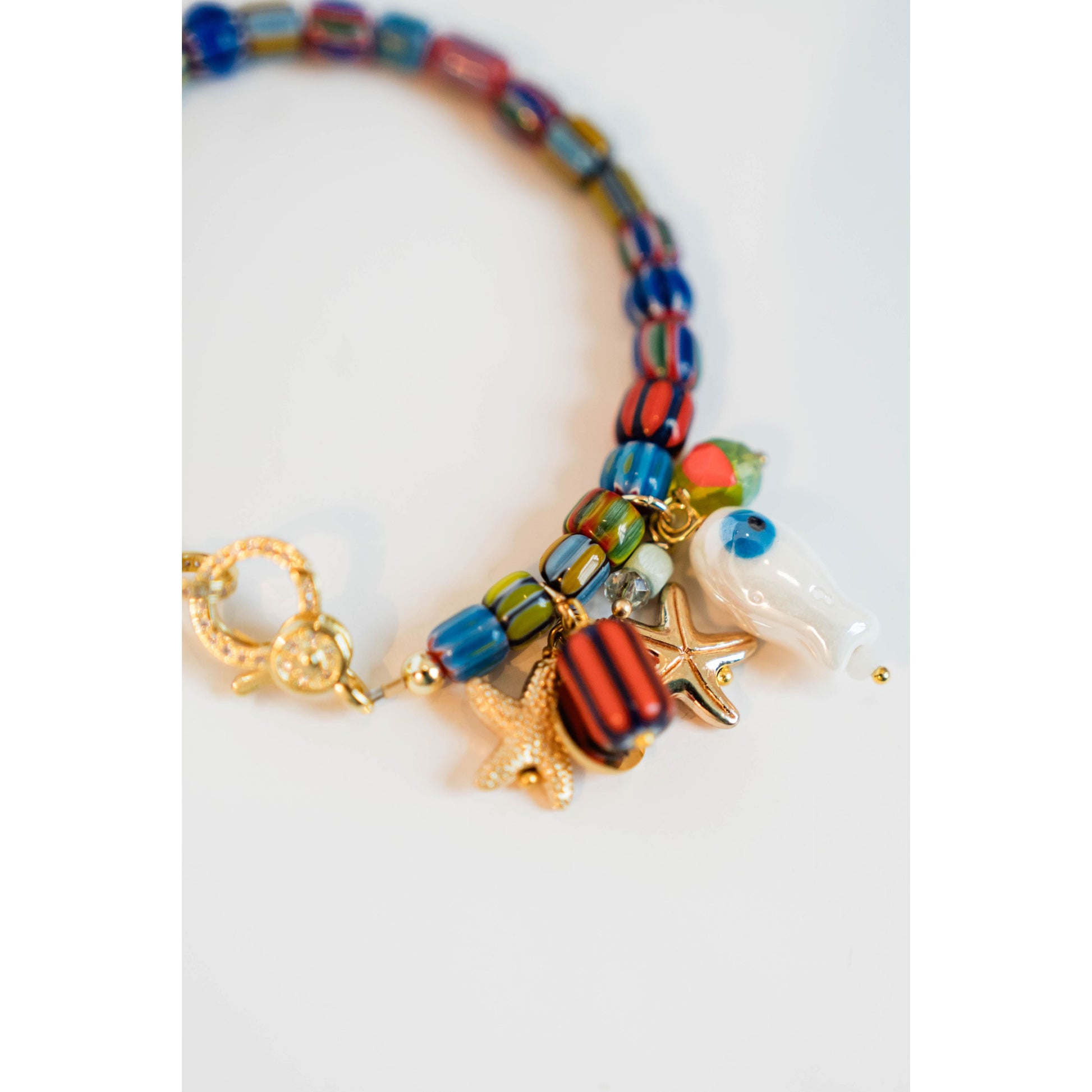 Colorful beaded bracelet with starfish and fish charms with a gold pave lever clasp on a white background