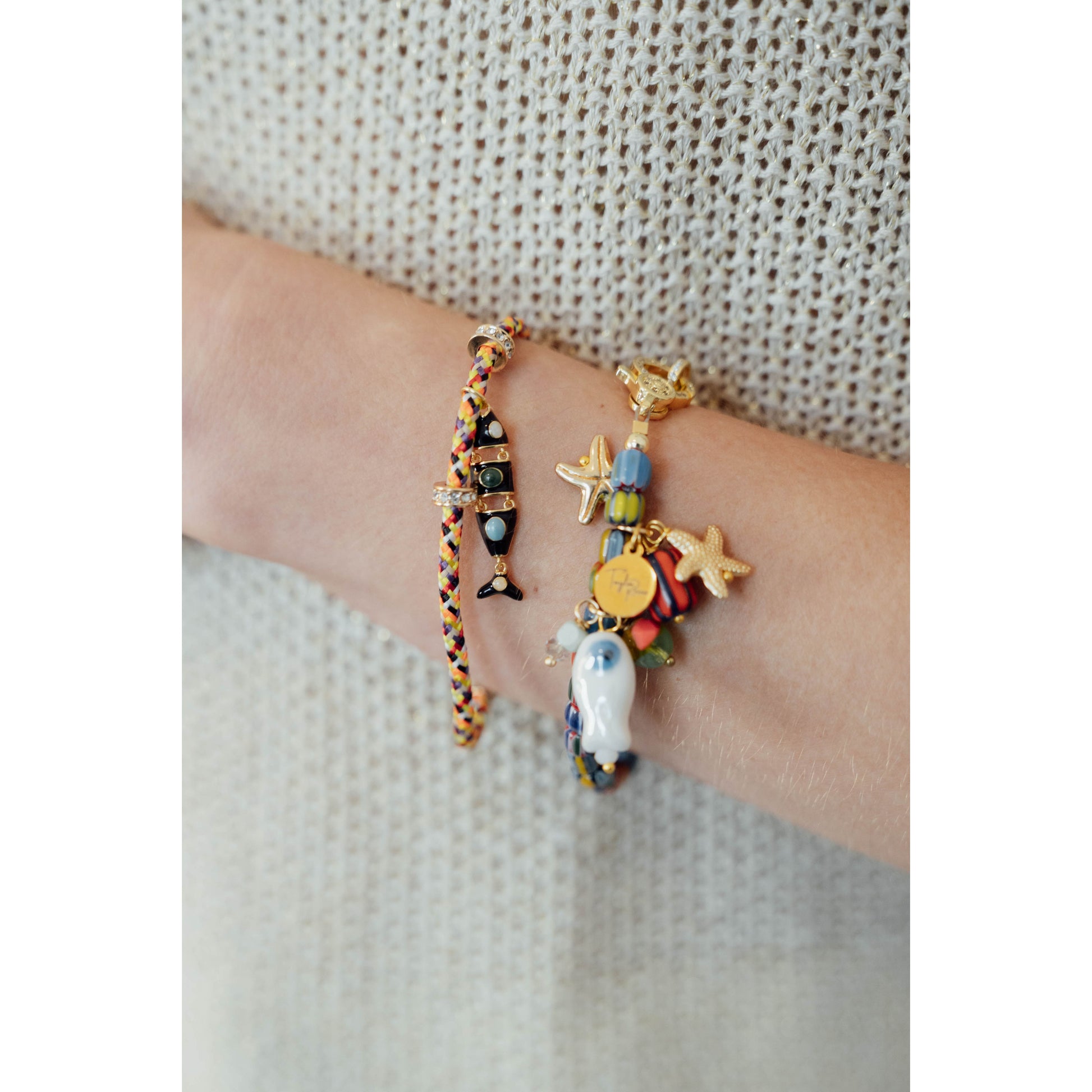 Multicolored bracelets with starfish and fish charms on a wrist against a neutral background