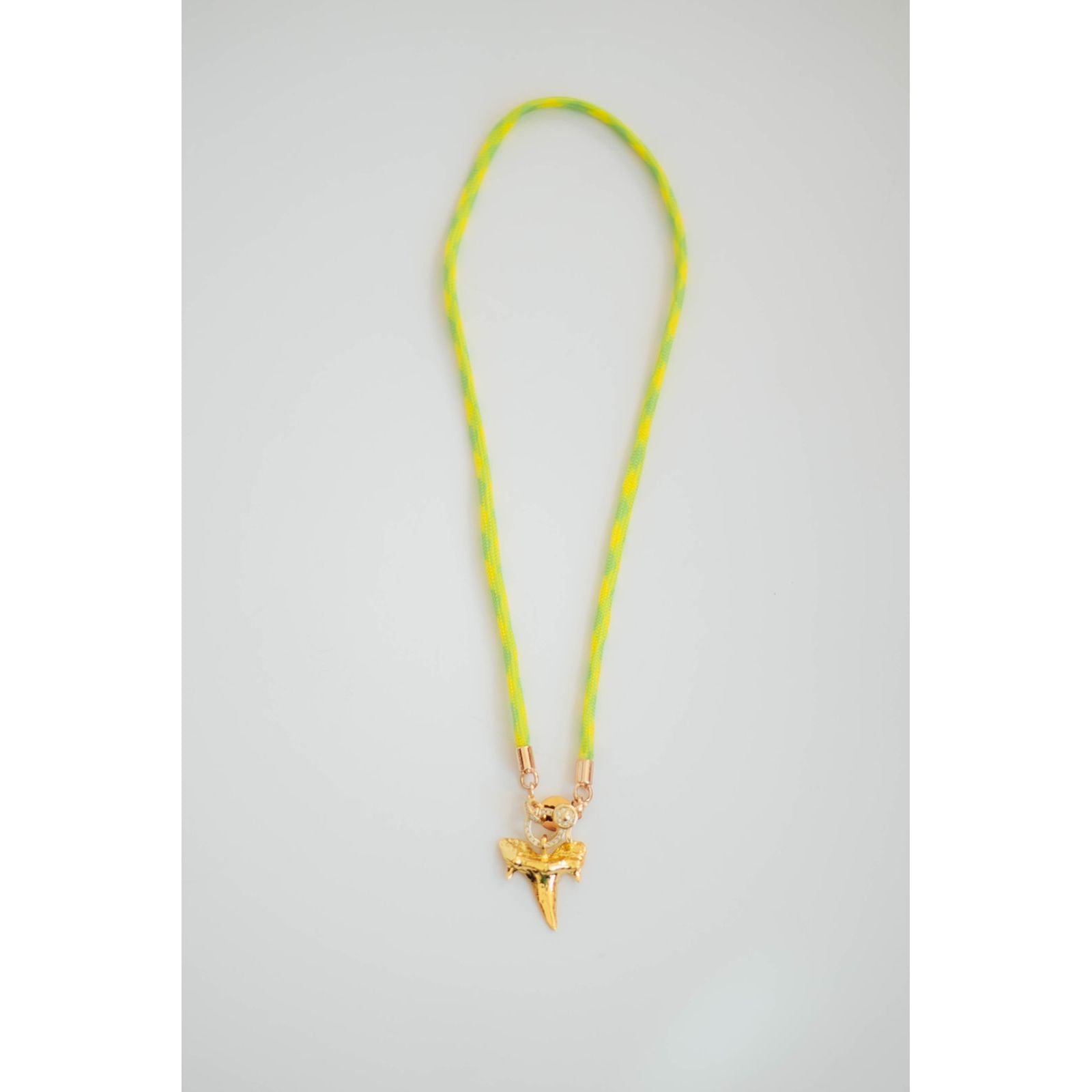Neon yellow and green cord necklace with a gold shark tooth pendant on a light gray background