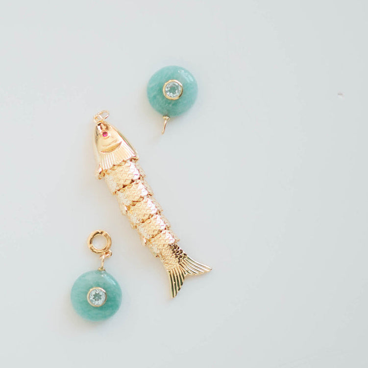 Pair of gold fish-shaped earrings with turquoise beads on a light blue background