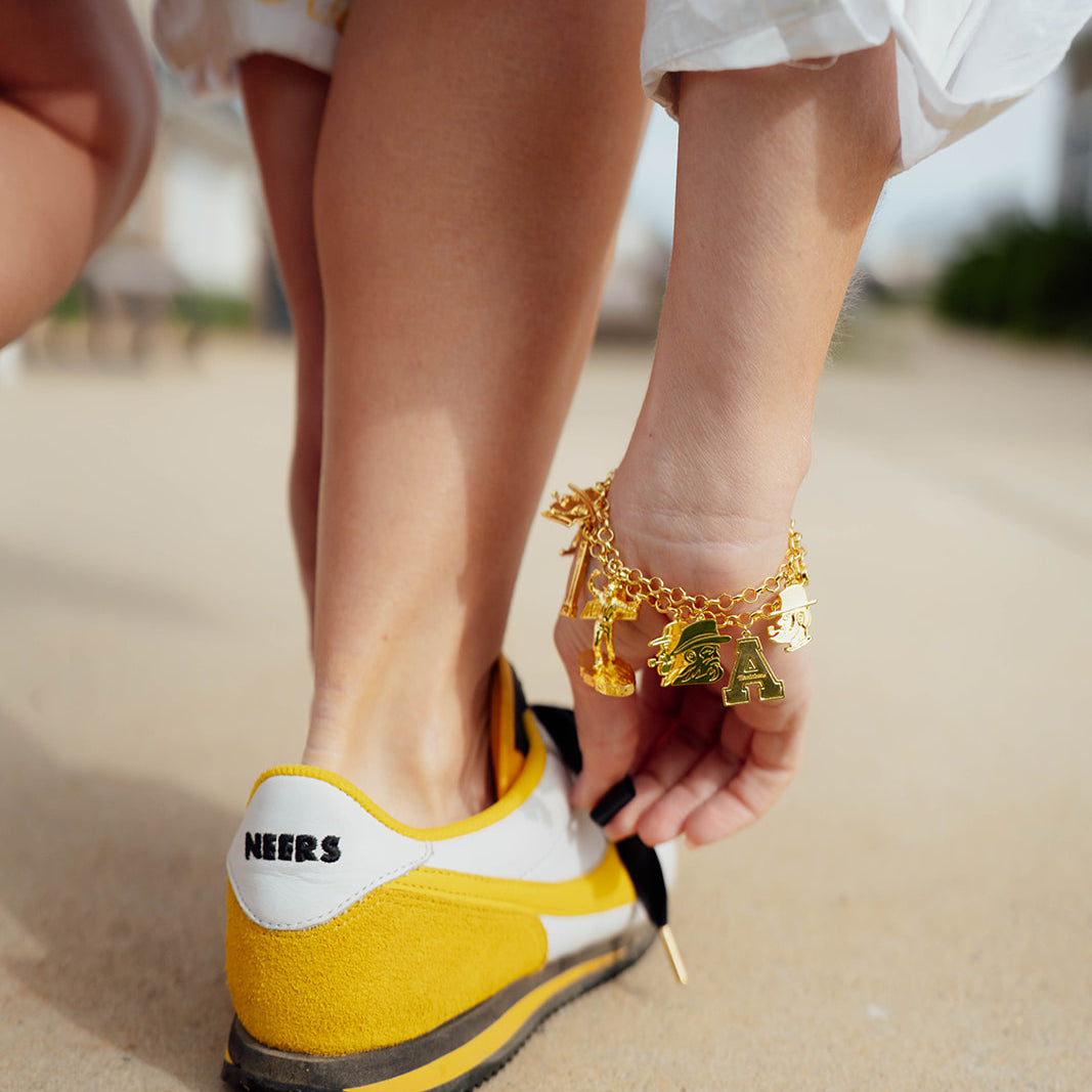 Person wearing a yellow shoe with 'Neers' branding on a sandy surface.