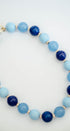 A beaded necklace made of alternating light blue and dark navy blue round beads, separated by small gold spacer beads, photographed on a clean white background.