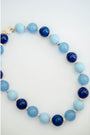 A beaded necklace made of alternating light blue and dark navy blue round beads, separated by small gold spacer beads, photographed on a clean white background.
