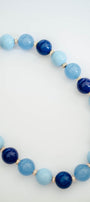 A beaded necklace made of alternating light blue and dark navy blue round beads, separated by small gold spacer beads, photographed on a clean white background.