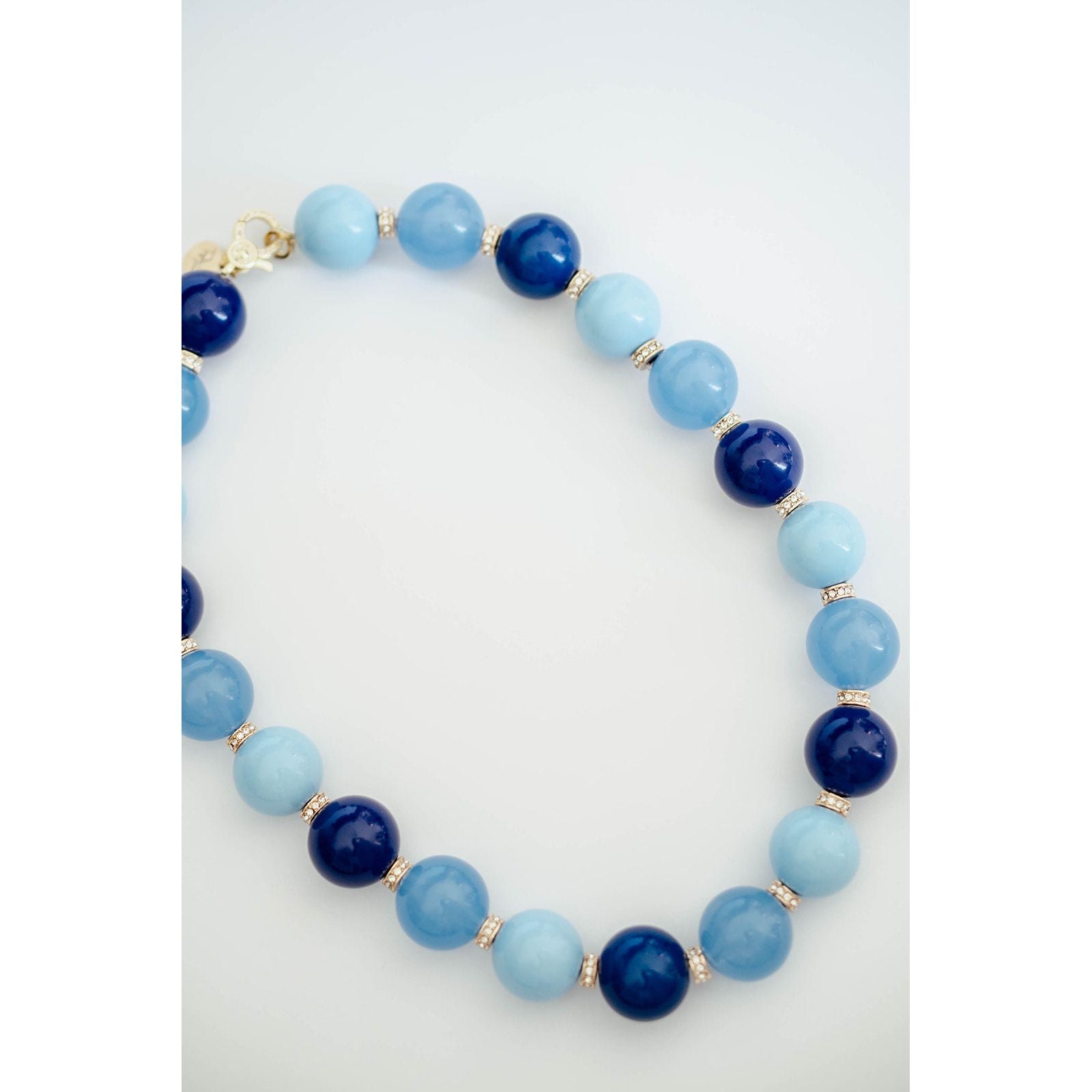 A beaded necklace made of alternating light blue and dark navy blue round beads, separated by small gold spacer beads, photographed on a clean white background.