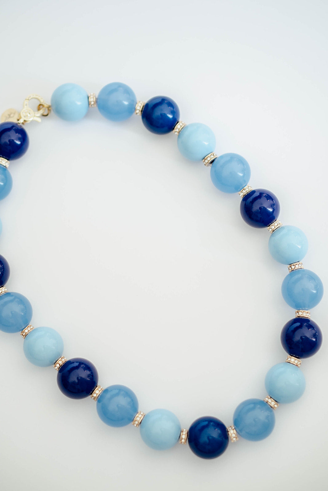 A beaded necklace made of alternating light blue and dark navy blue round beads, separated by small gold spacer beads, photographed on a clean white background.