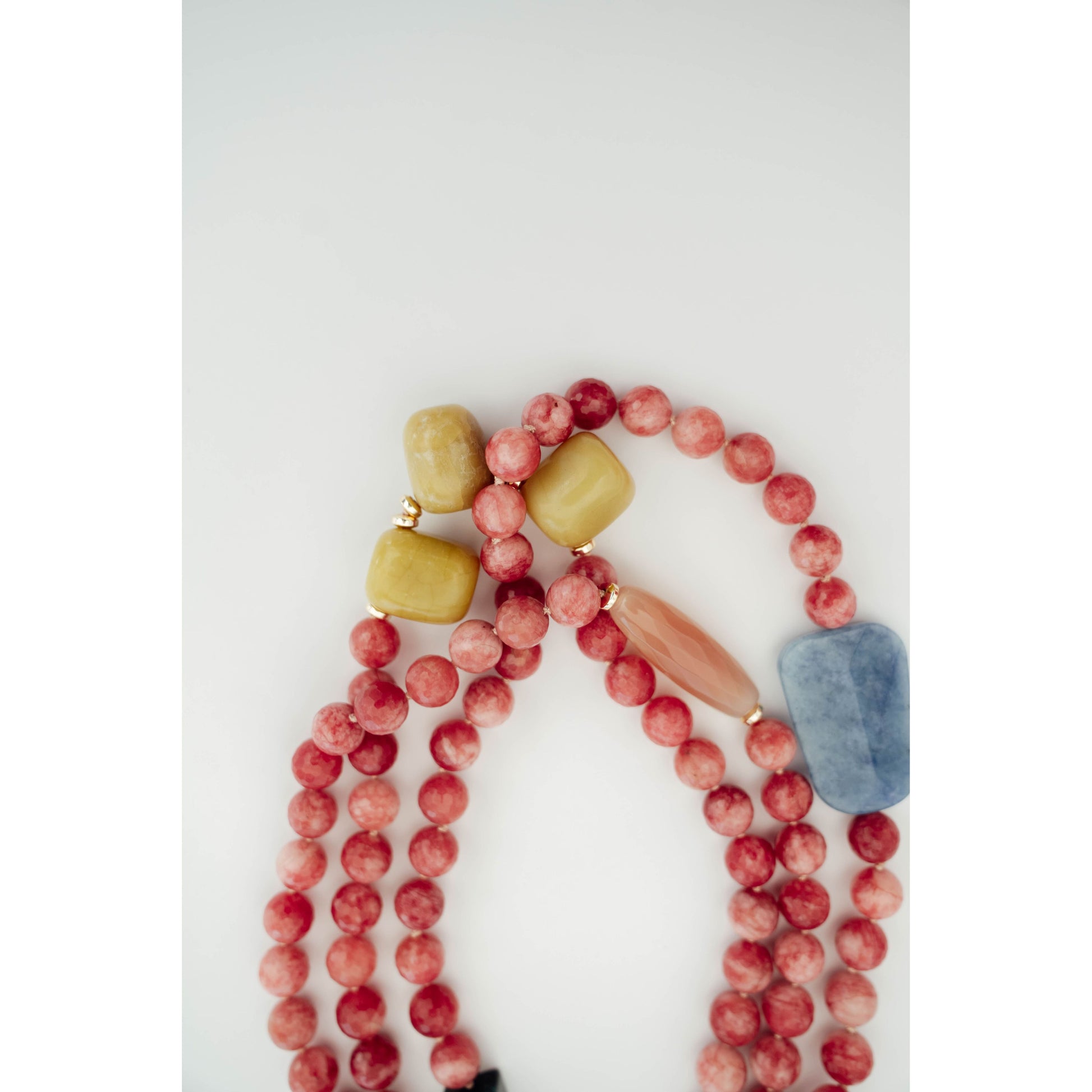 A beaded necklace with round pinkish-red beads, a light blue stone bead, and three textured yellow-green accent beads, arranged on a plain white background.