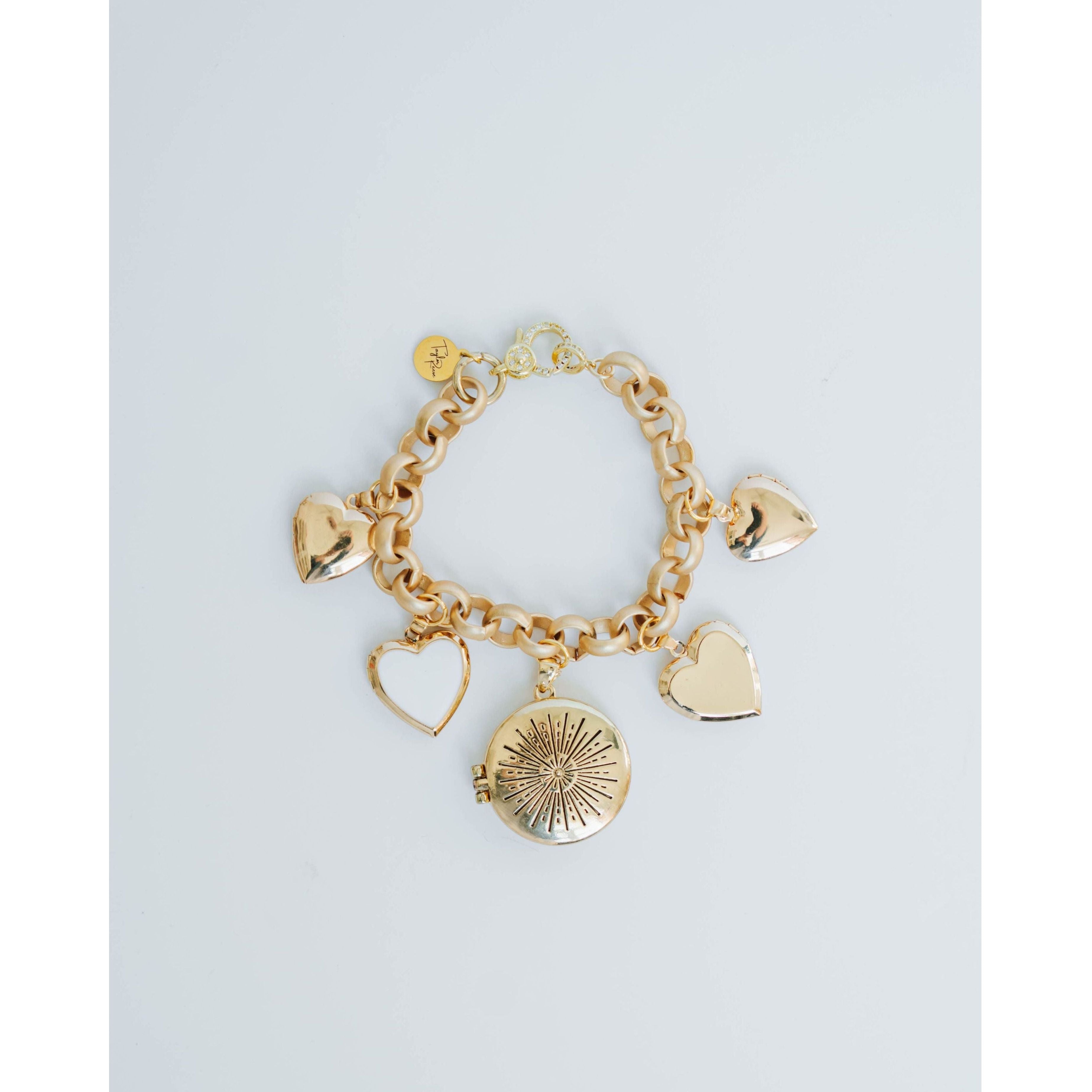 Gold bracelet with heart and round charm on a light gray background