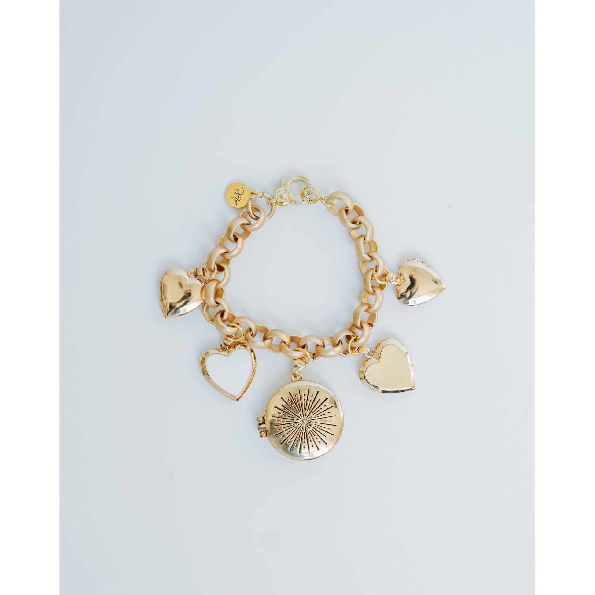 Gold bracelet with heart and round charm on a light gray background