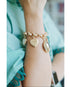 Gold bracelet with heart-shaped charms on a wrist, wearing a light blue garment.