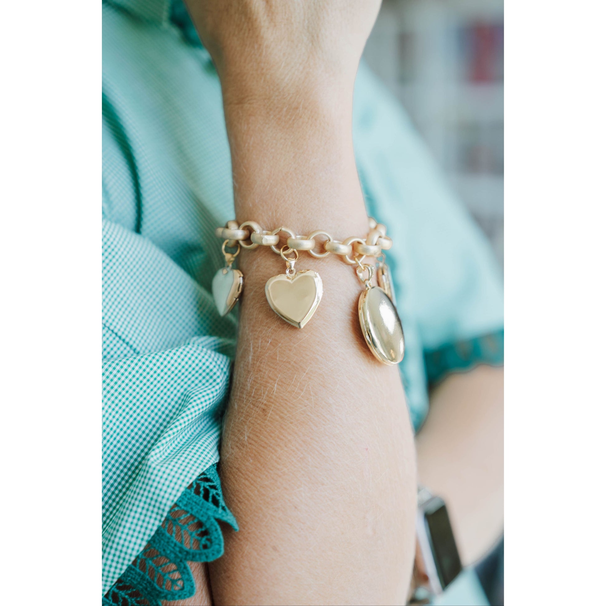 Gold bracelet with heart-shaped charms on a wrist, wearing a light blue garment.