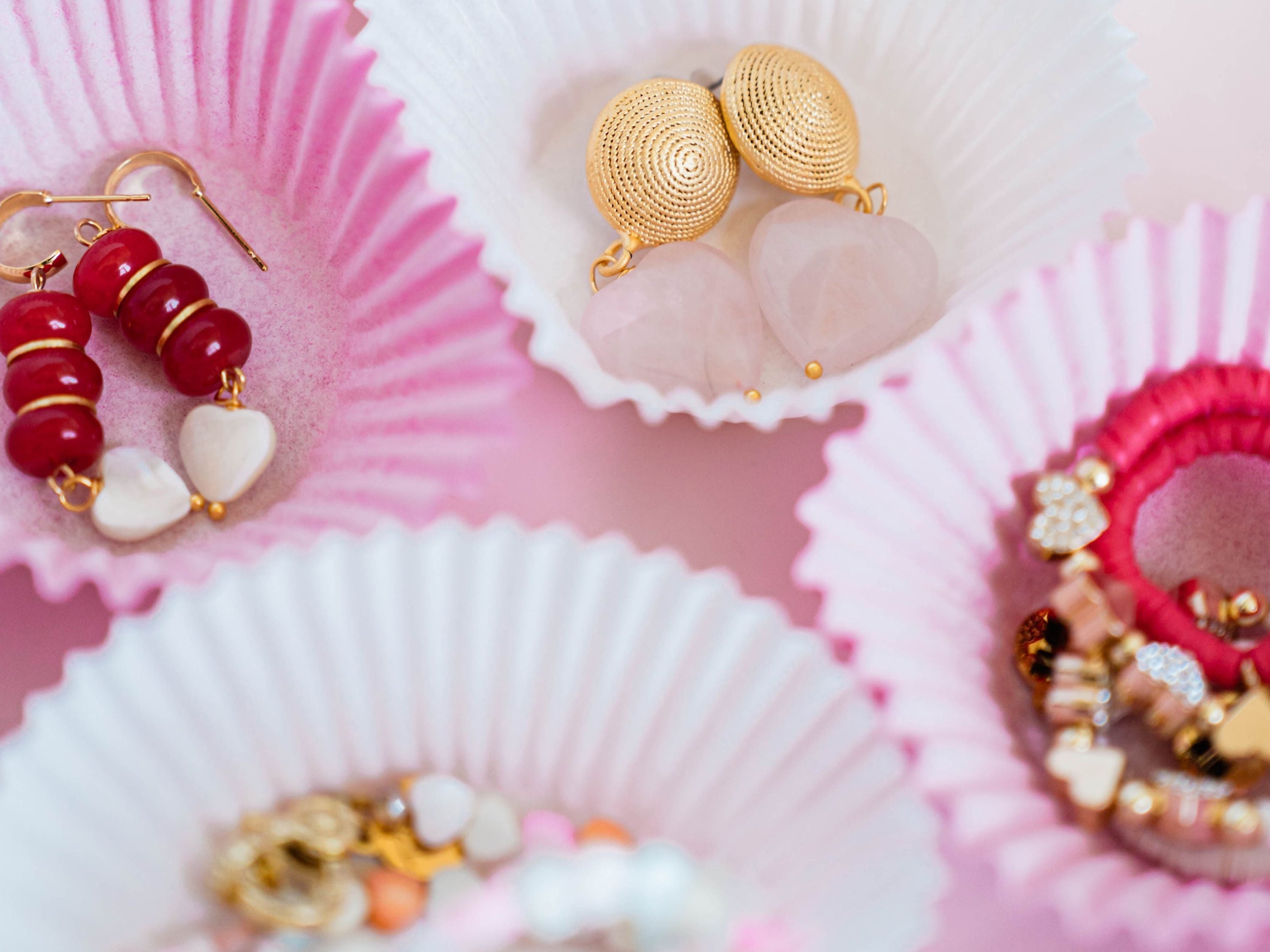 Gold and colorful beaded earrings displayed in pink and white cupcake liners.