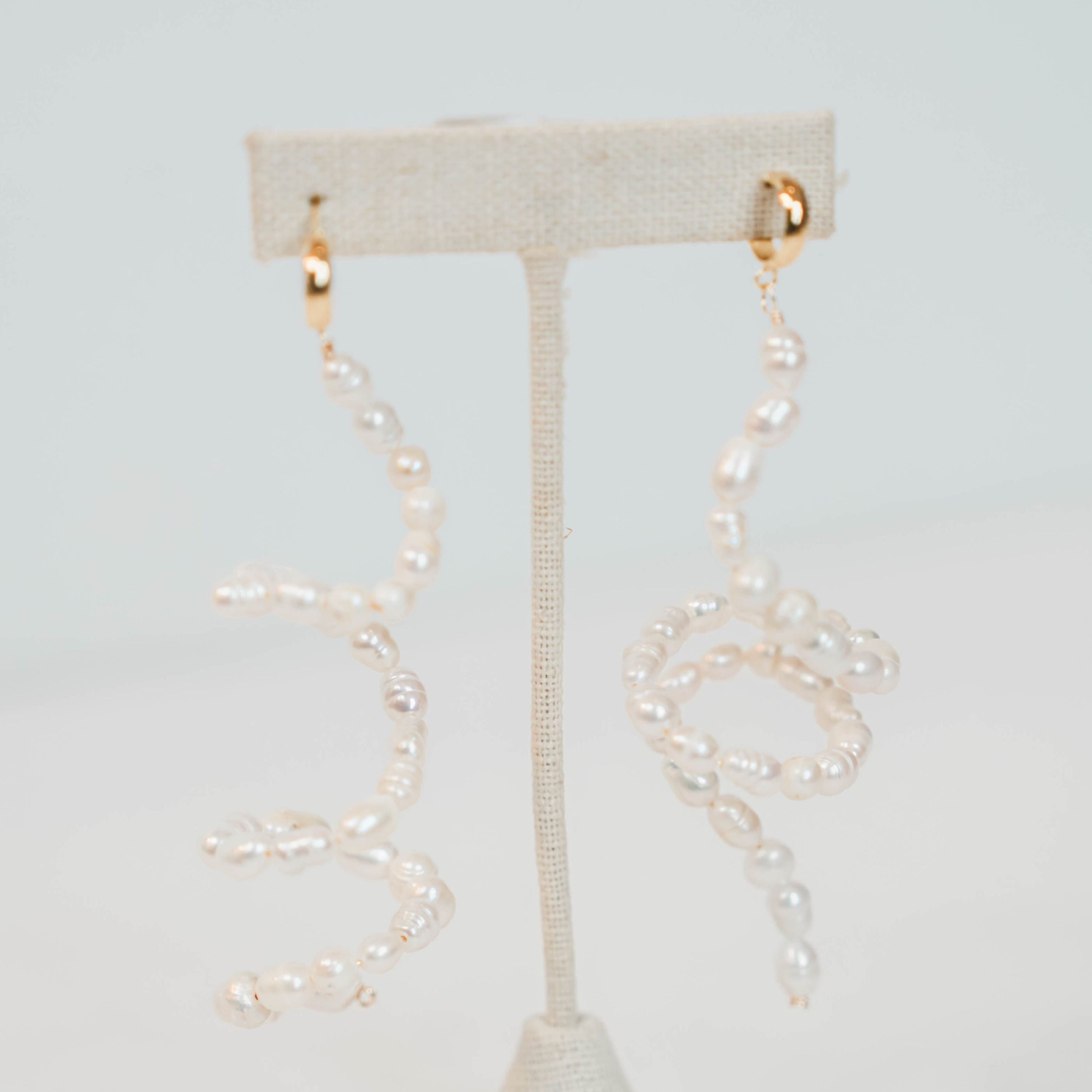 Pearl earrings on a white stand against a light gray background