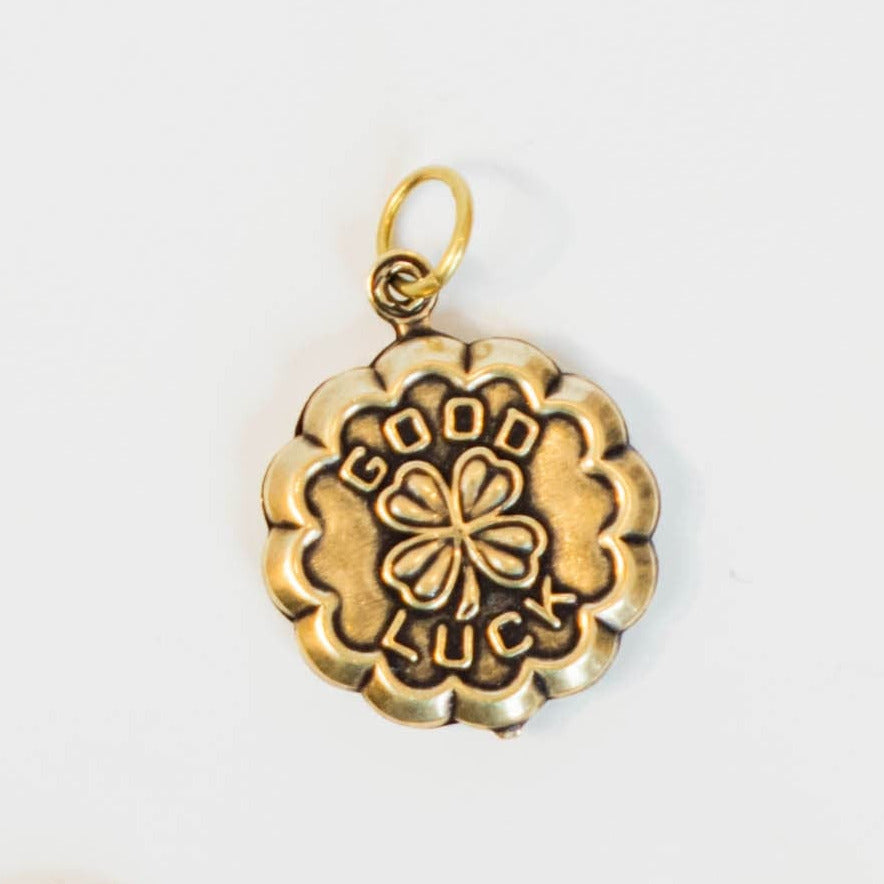 gold and brass charm with "good luck" engraved and a 4 leaf clover in the center on a light background