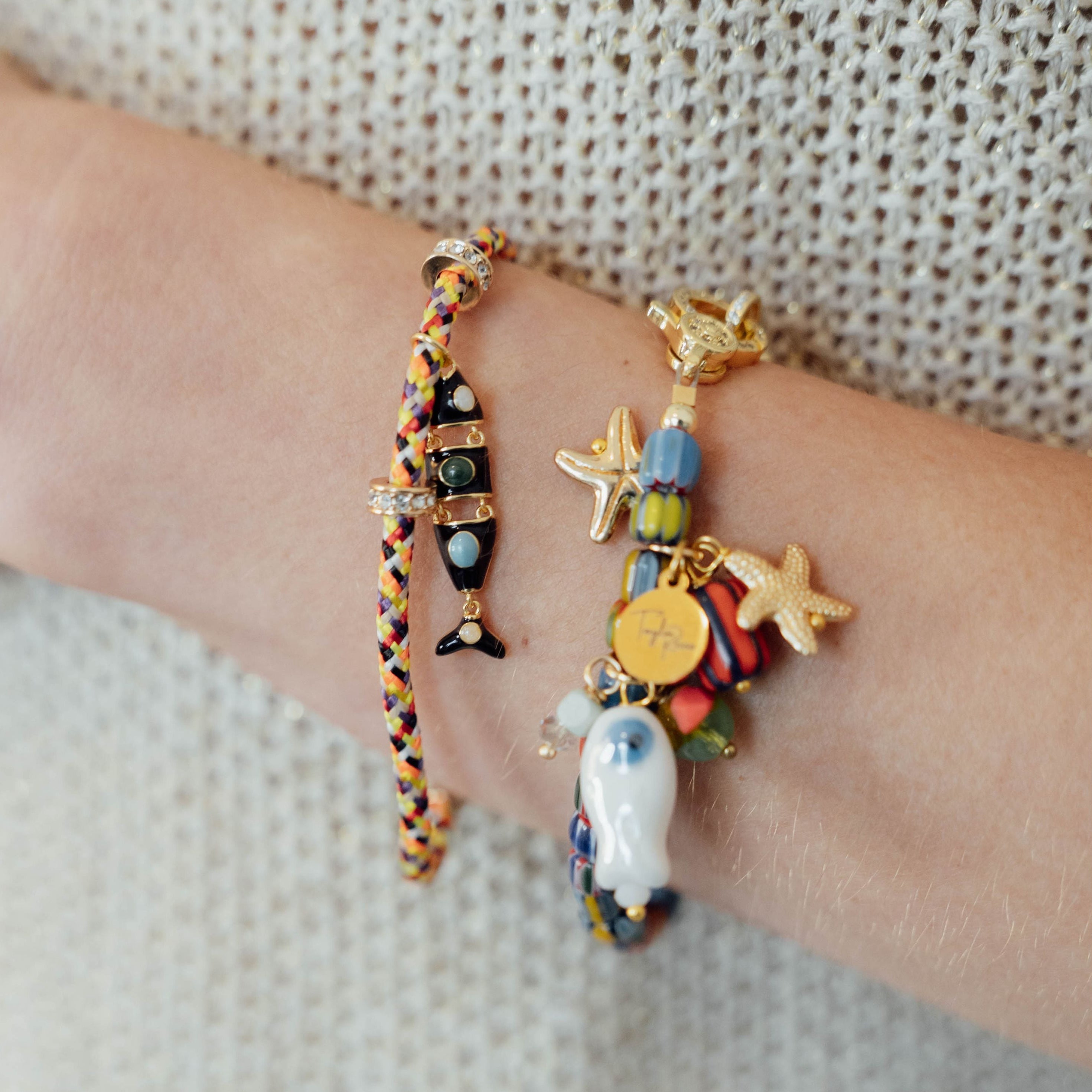 Bracelets with colorful charms on a wrist against a neutral background