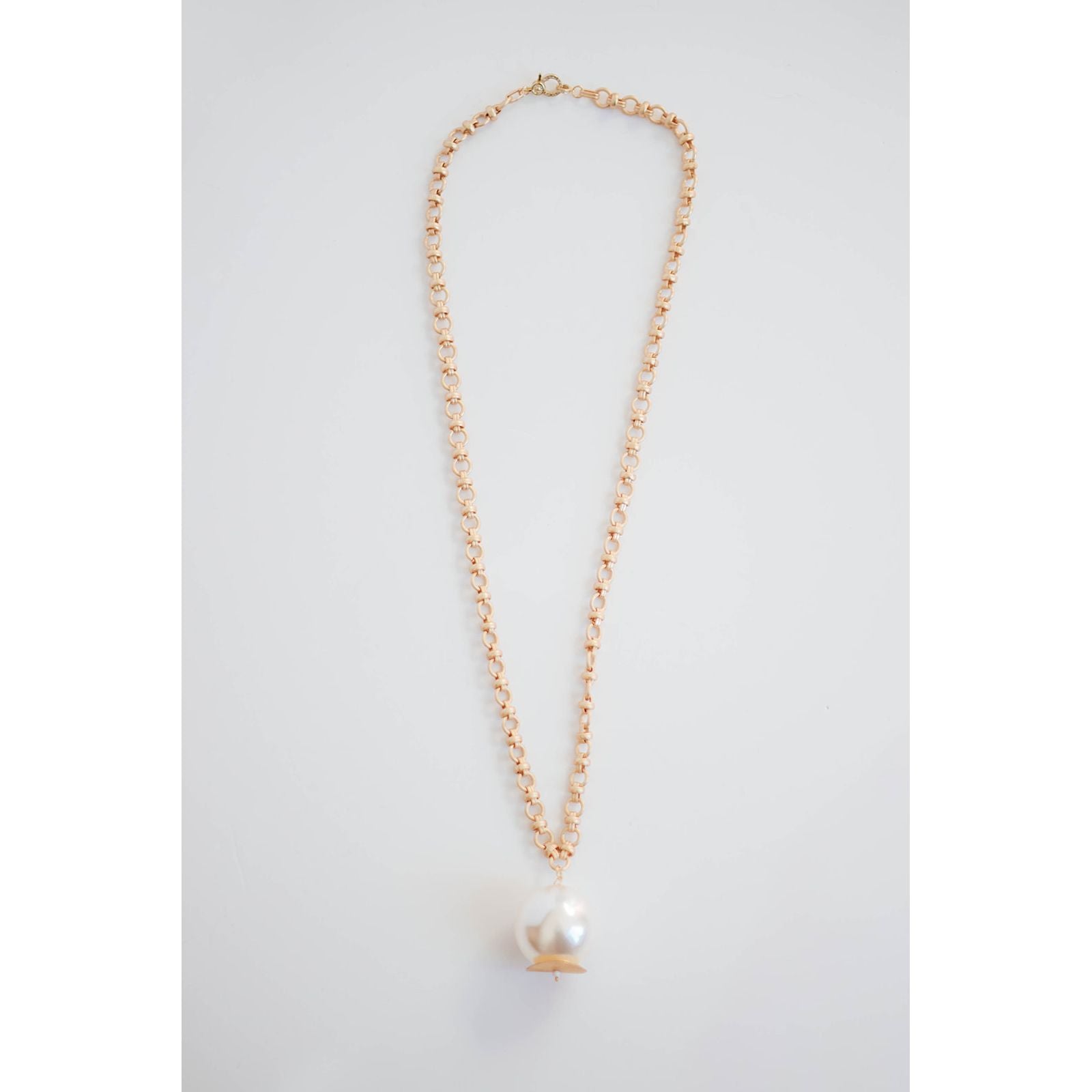 thick gold chain necklace with an oversized pearl pendant on a light grey background