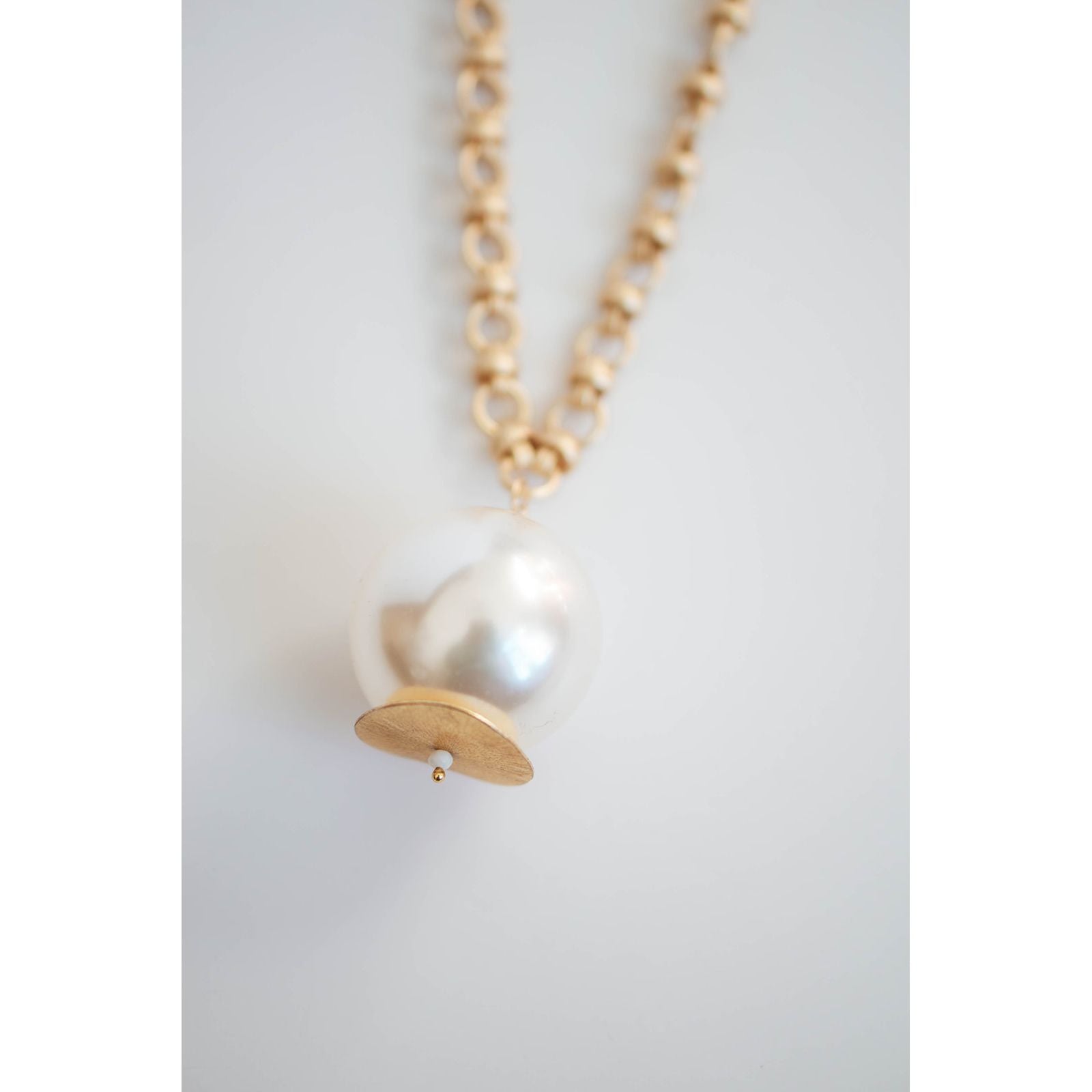 close-up shot of an oversized pearl pendant on a gold chain necklace on  a light grey background