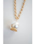 close-up shot of an oversized pearl pendant on a gold chain necklace on  a light grey background
