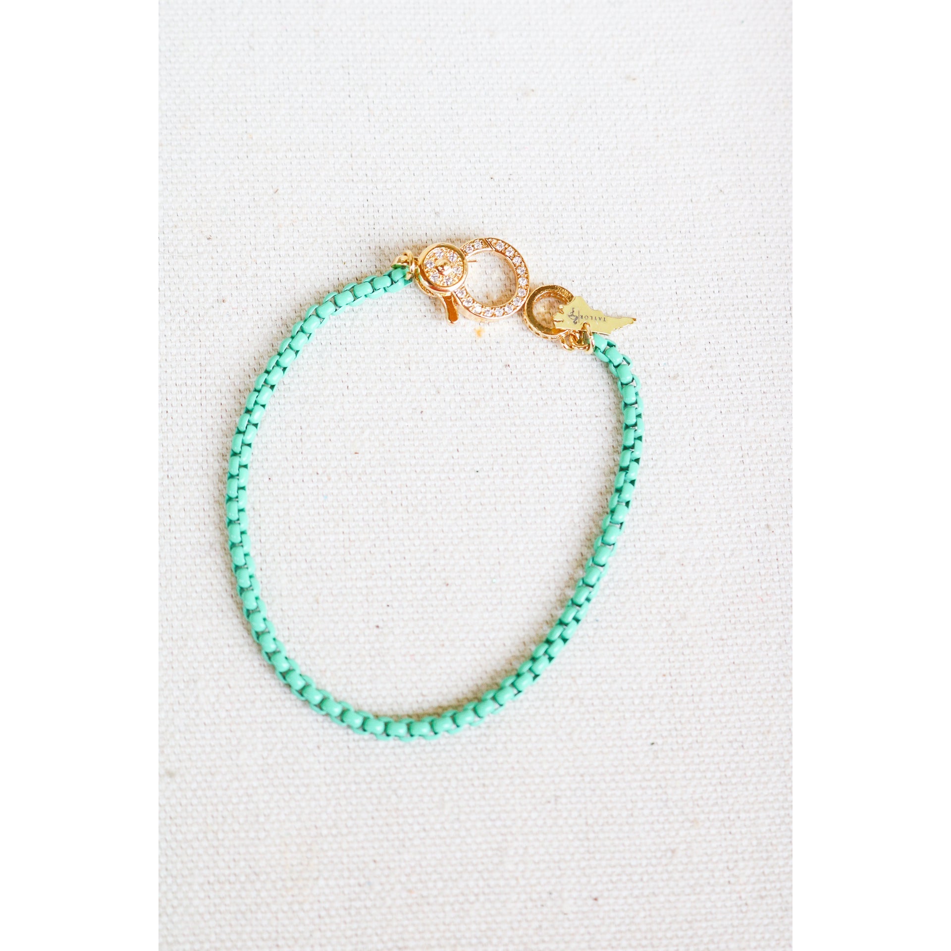 mint green box chain bracelet with a gold pave lever clasp on a light grey background