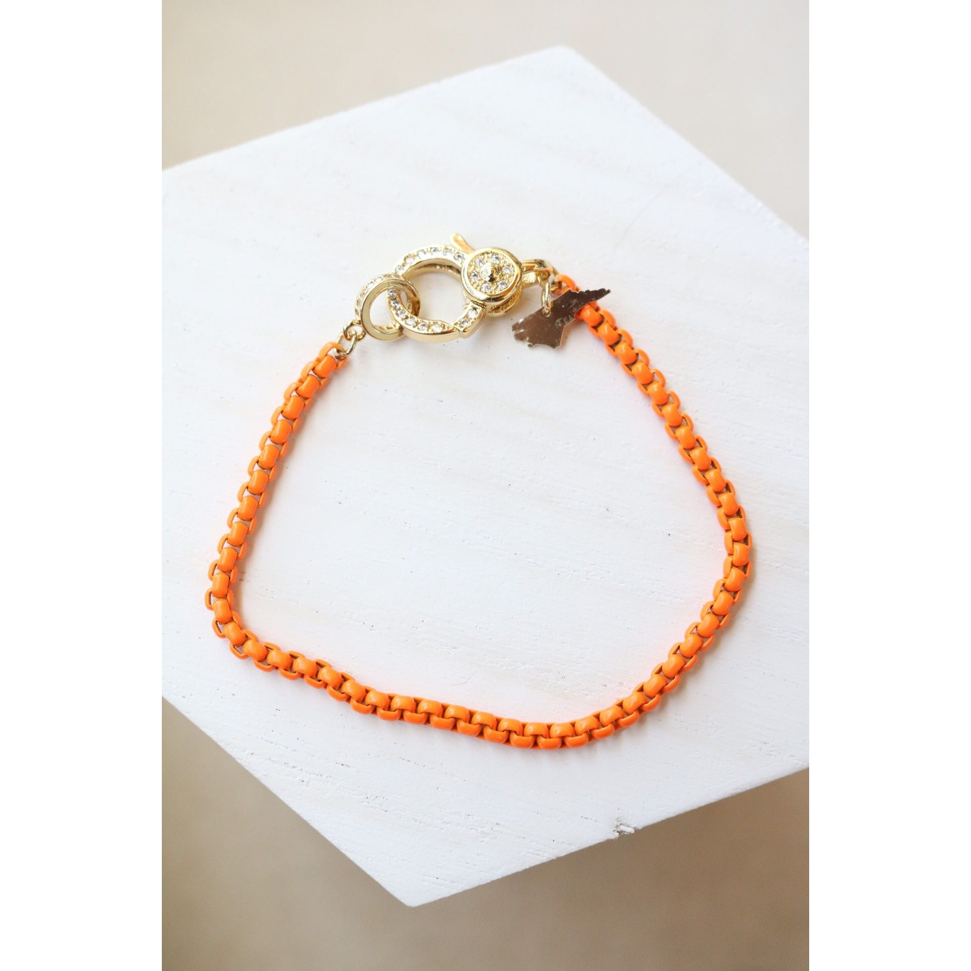 orange colored box chain bracelet with a gold pave lever clasp on a light background