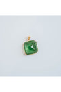 square-shaped pendant with a green crystal gem in a gold-toned brass frame against a light background