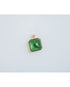 square-shaped pendant with a green crystal gem in a gold-toned brass frame against a light background