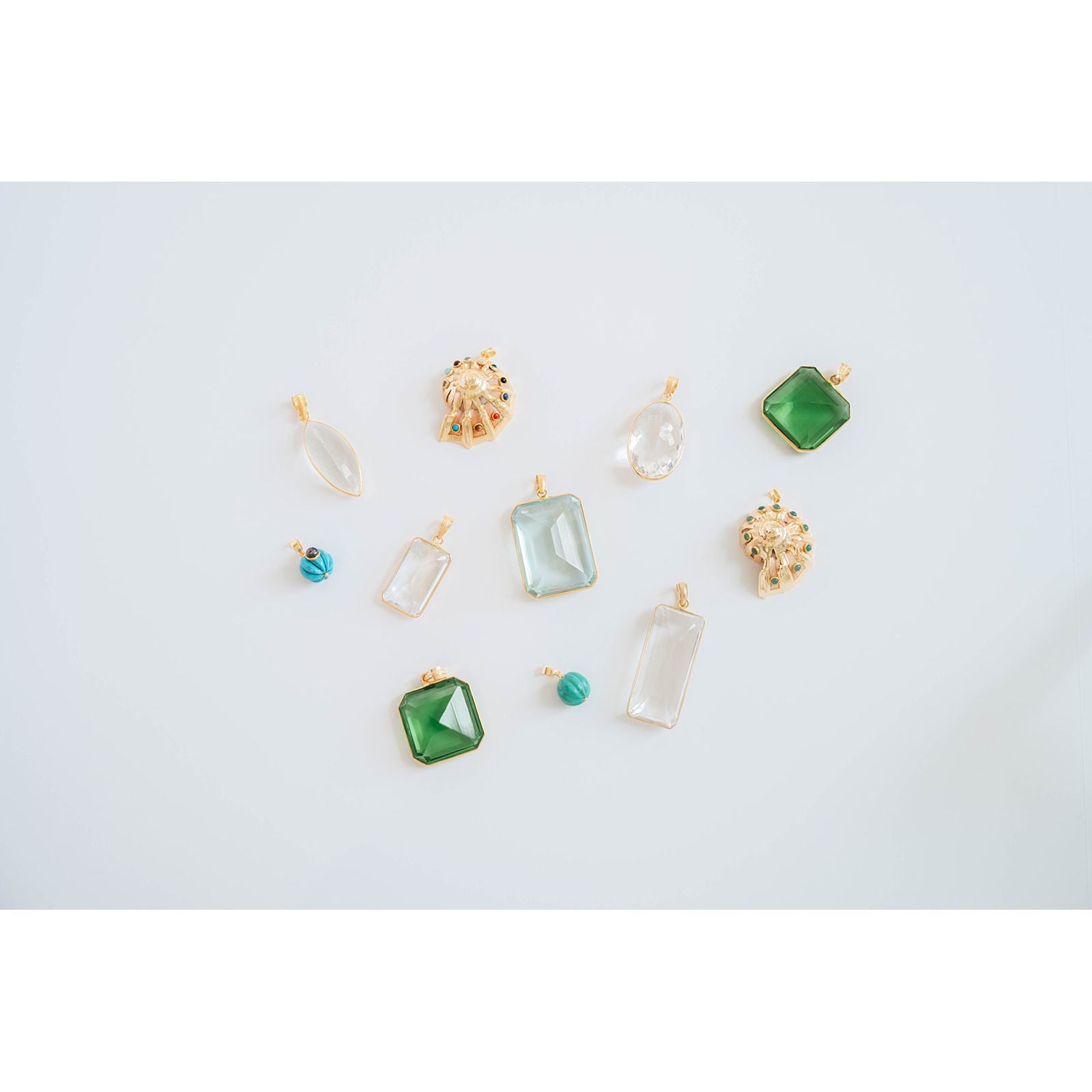 Collection of various gemstone pendants in light blue, crystal, and green on a light gray background