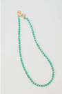 Turquoise beaded necklace with a gold pave lever clasp on a light gray background