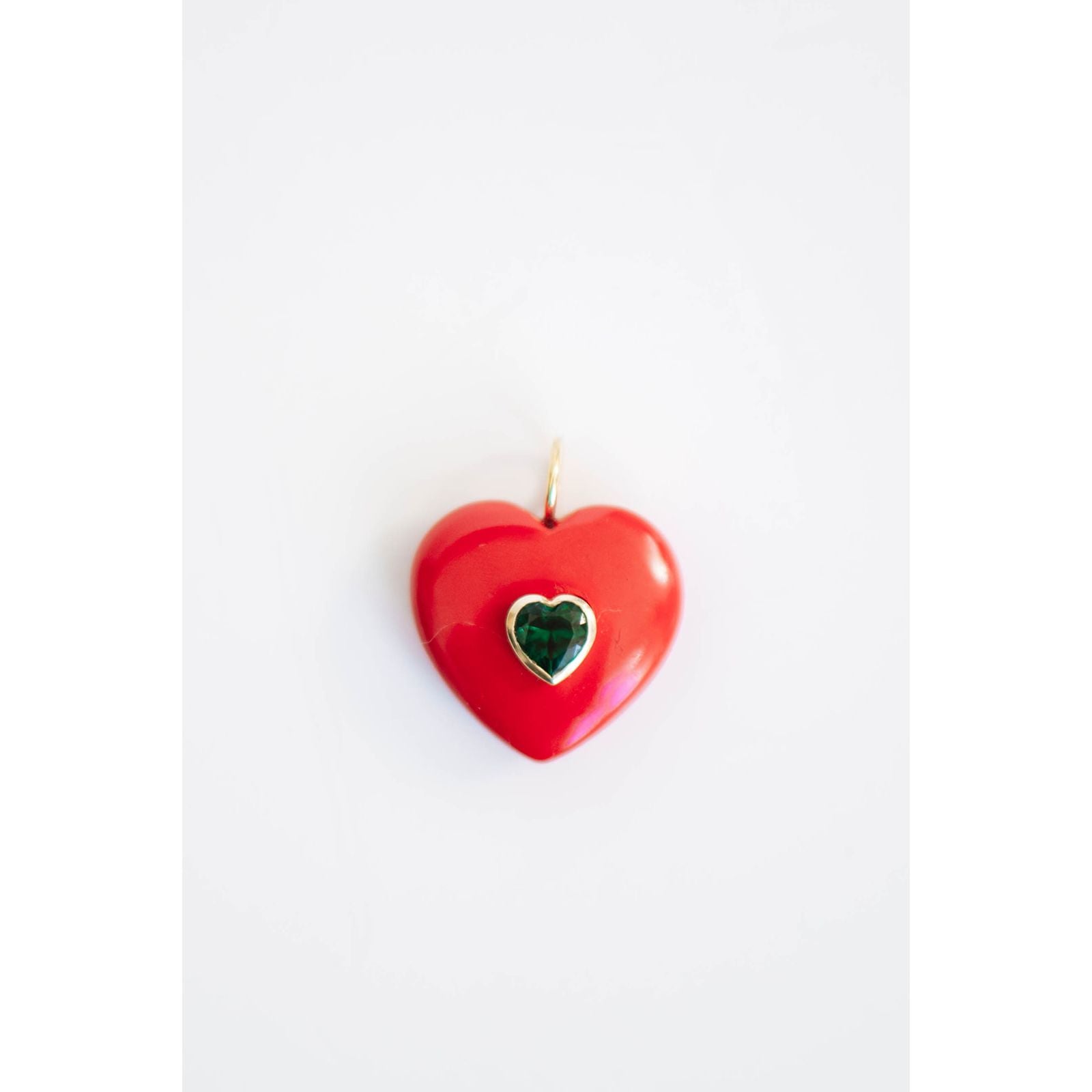 Red heart-shaped pendant with a green crystal center gemstone on a light background