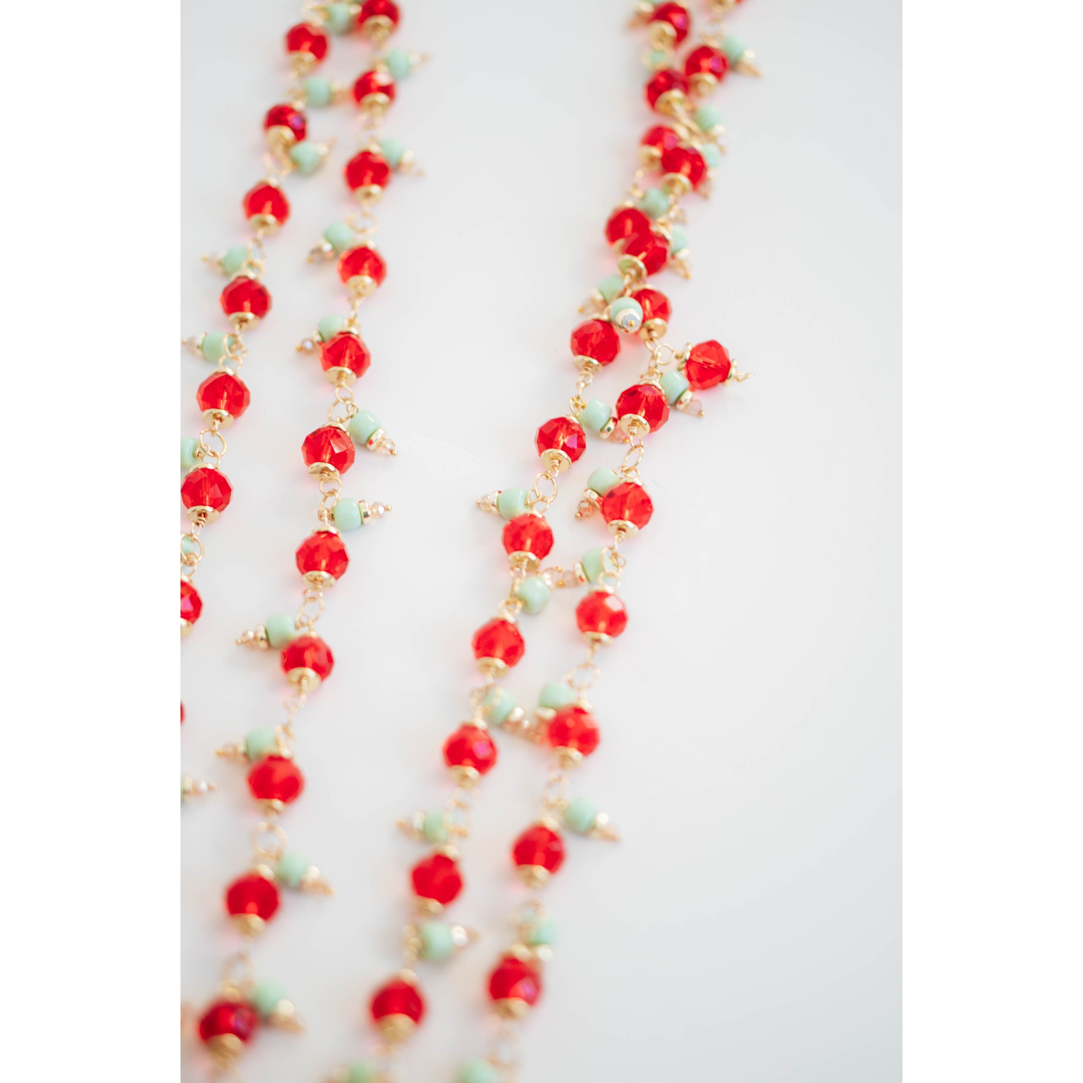 Necklace with red crystal, mint green, and gold beads on a white background