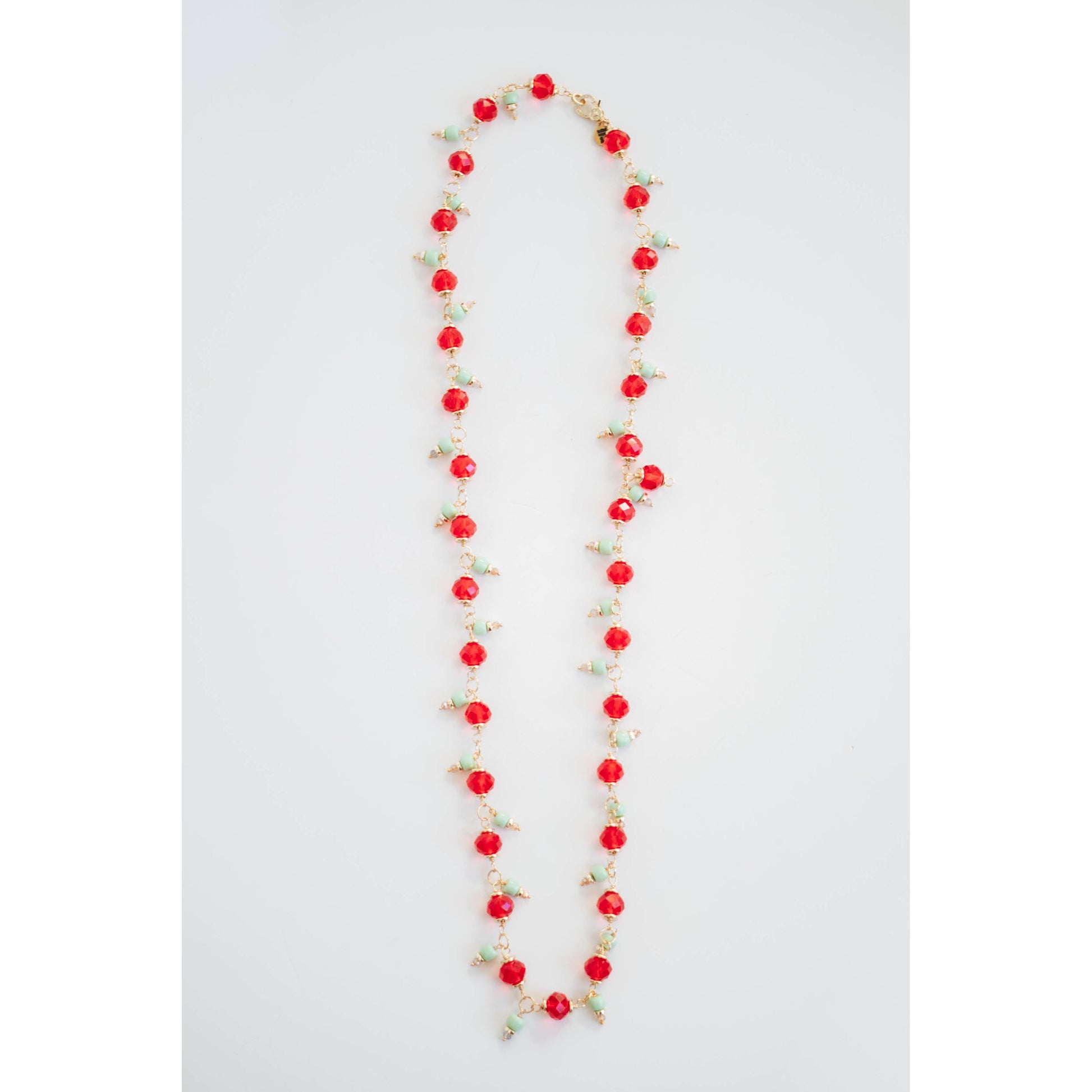 Long necklace with red crystal beads and mint green and gold accents on a light gray background