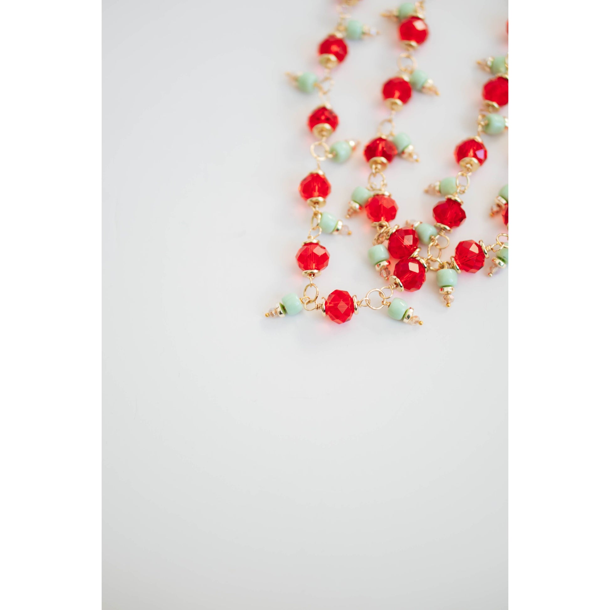 Necklace with red crystal and mint green and gold beads on a white background