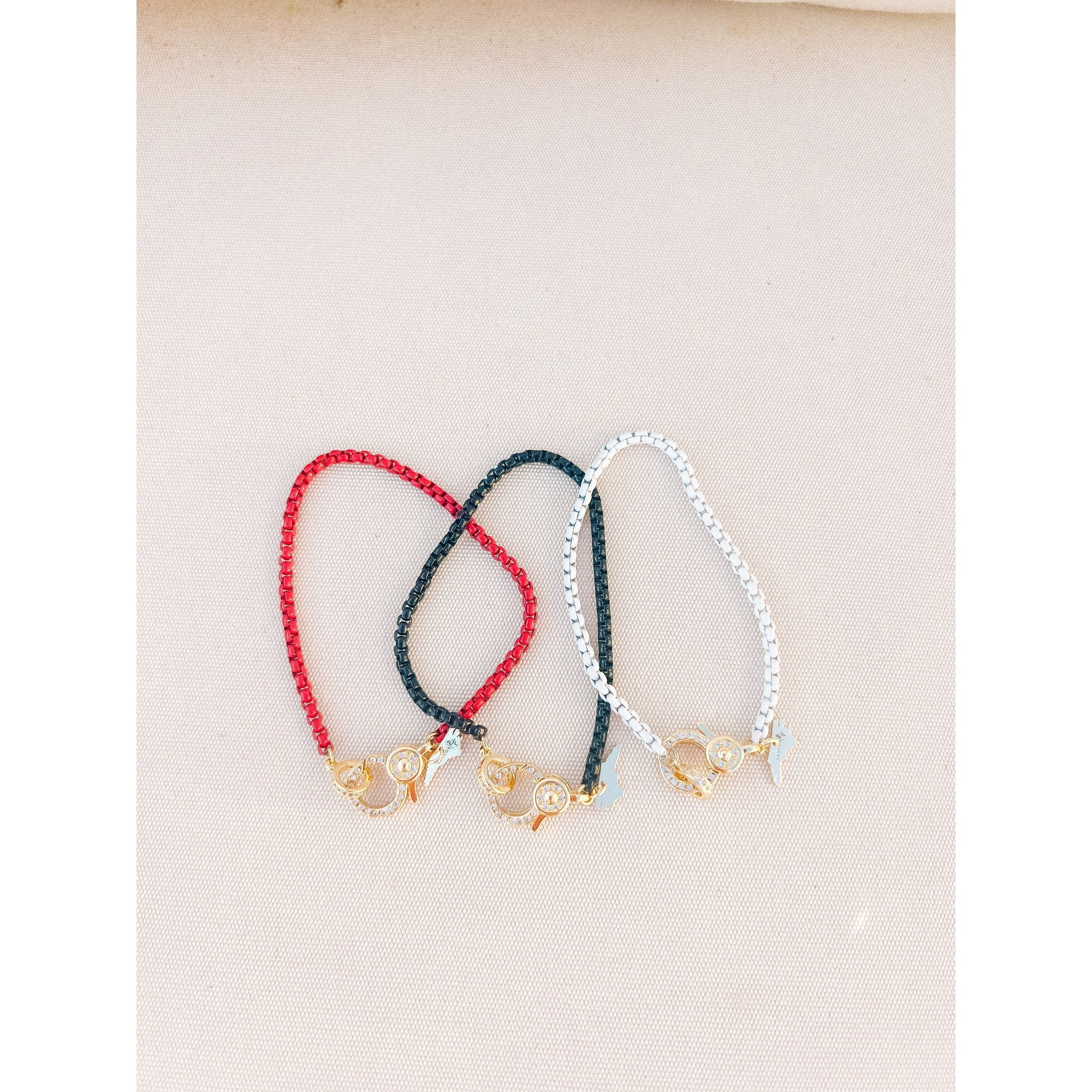 set of 3 overlapping box chain bracelets in red, black, and white with gold pave lever clasps on a light background