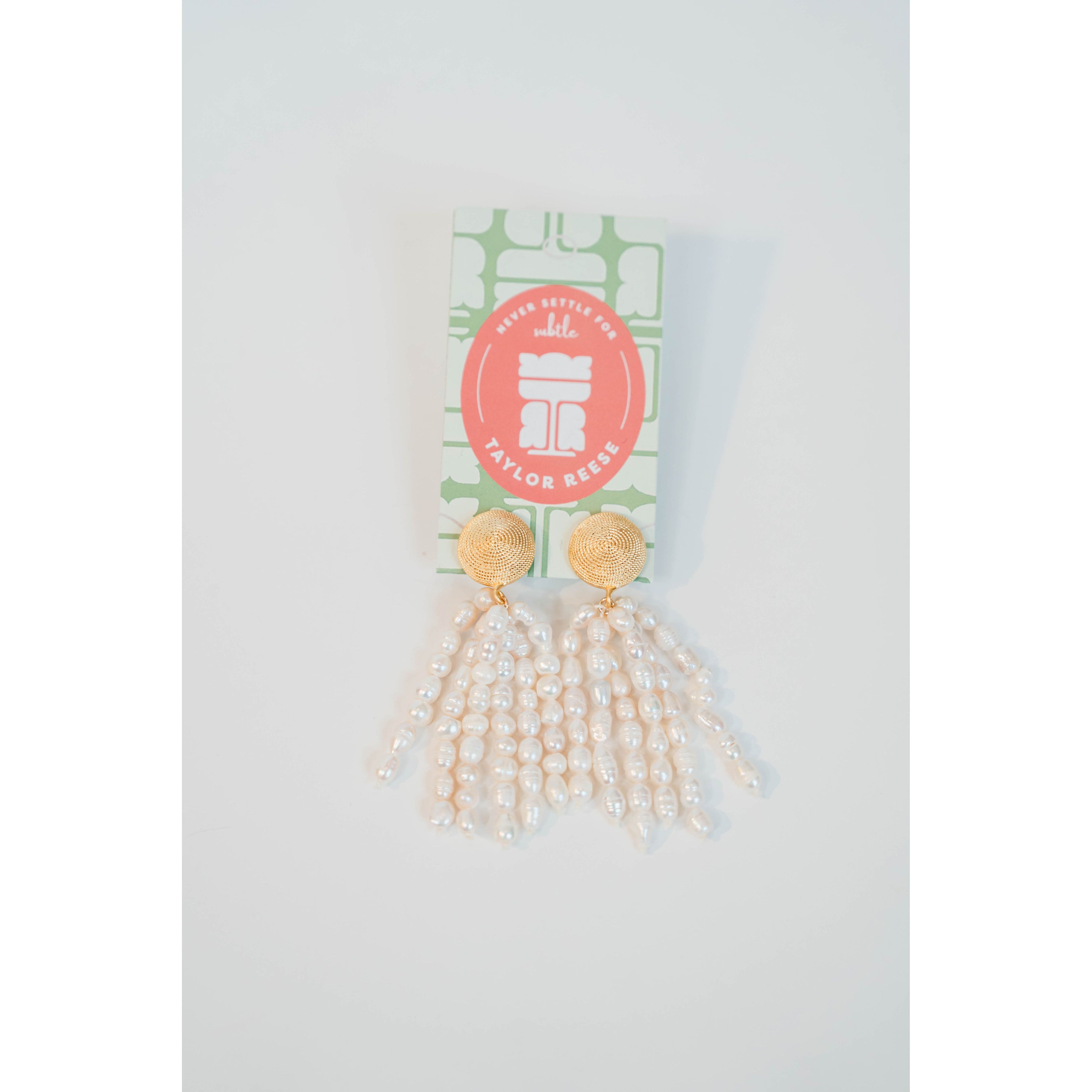 Gold and pearl tassel earrings on a white background with a visible brand label.