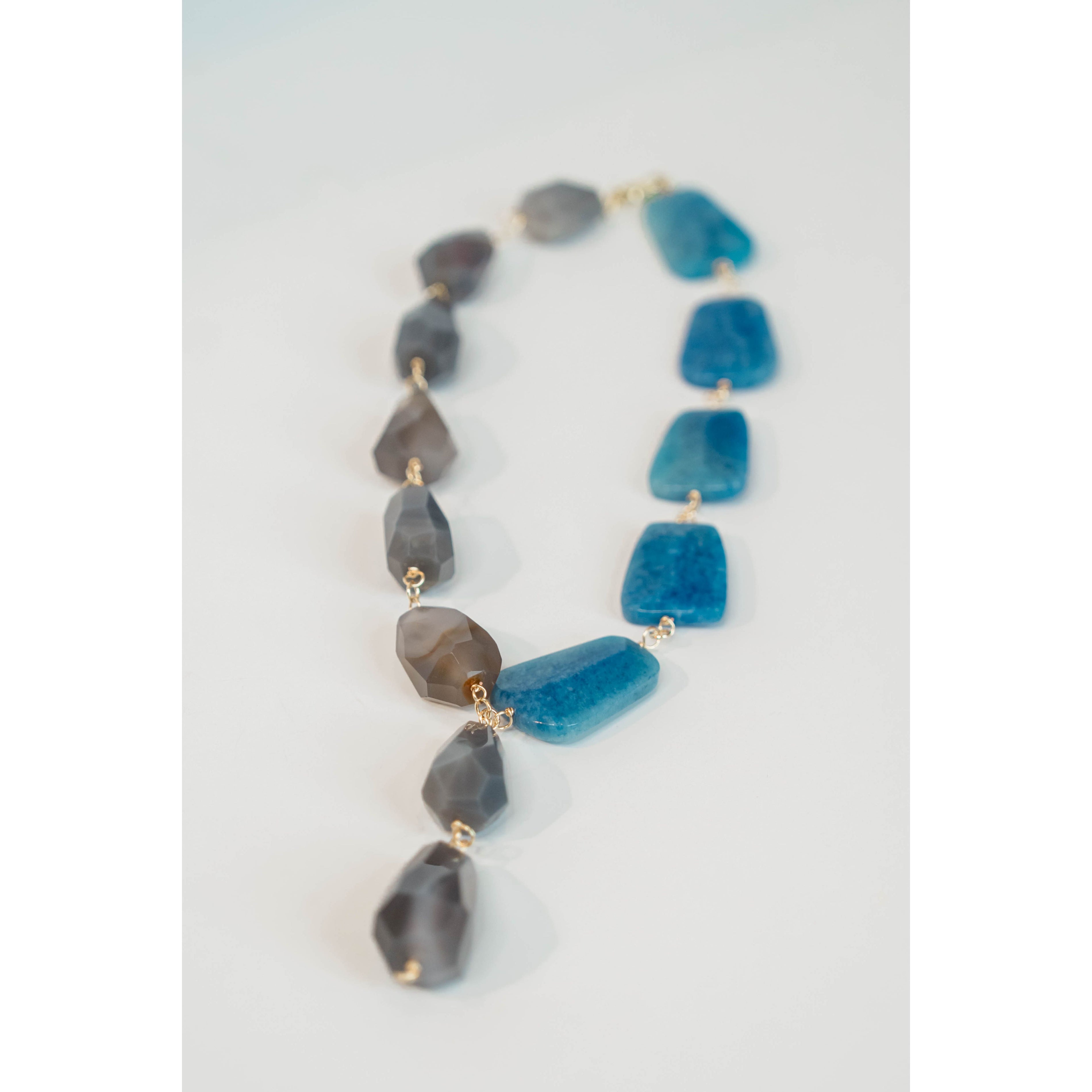 statement necklace with gold chain and blue and grey stone accents on a light grey background