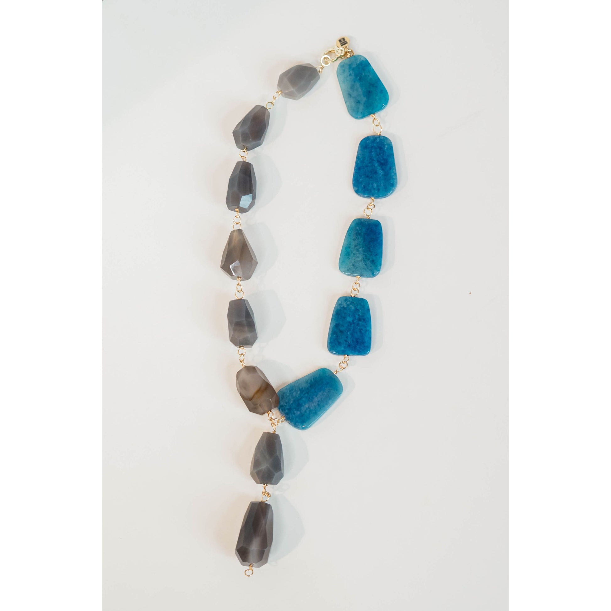statement necklace with gold chain and blue and grey stone accents on a light grey background