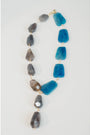 statement necklace with gold chain and blue and grey stone accents on a light grey background